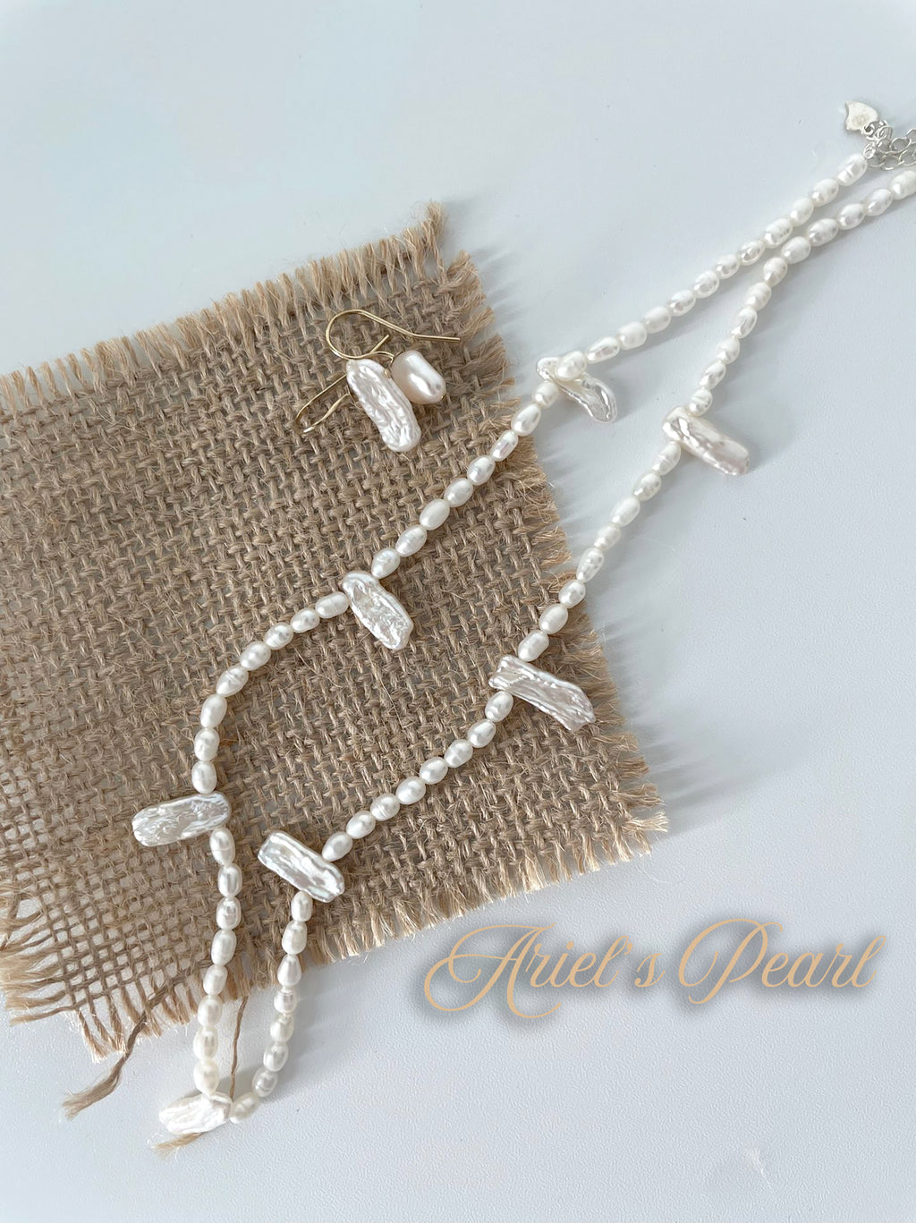 Pearl necklace and earrings on a textured fabric with 'Ariel's Pearl' branding.