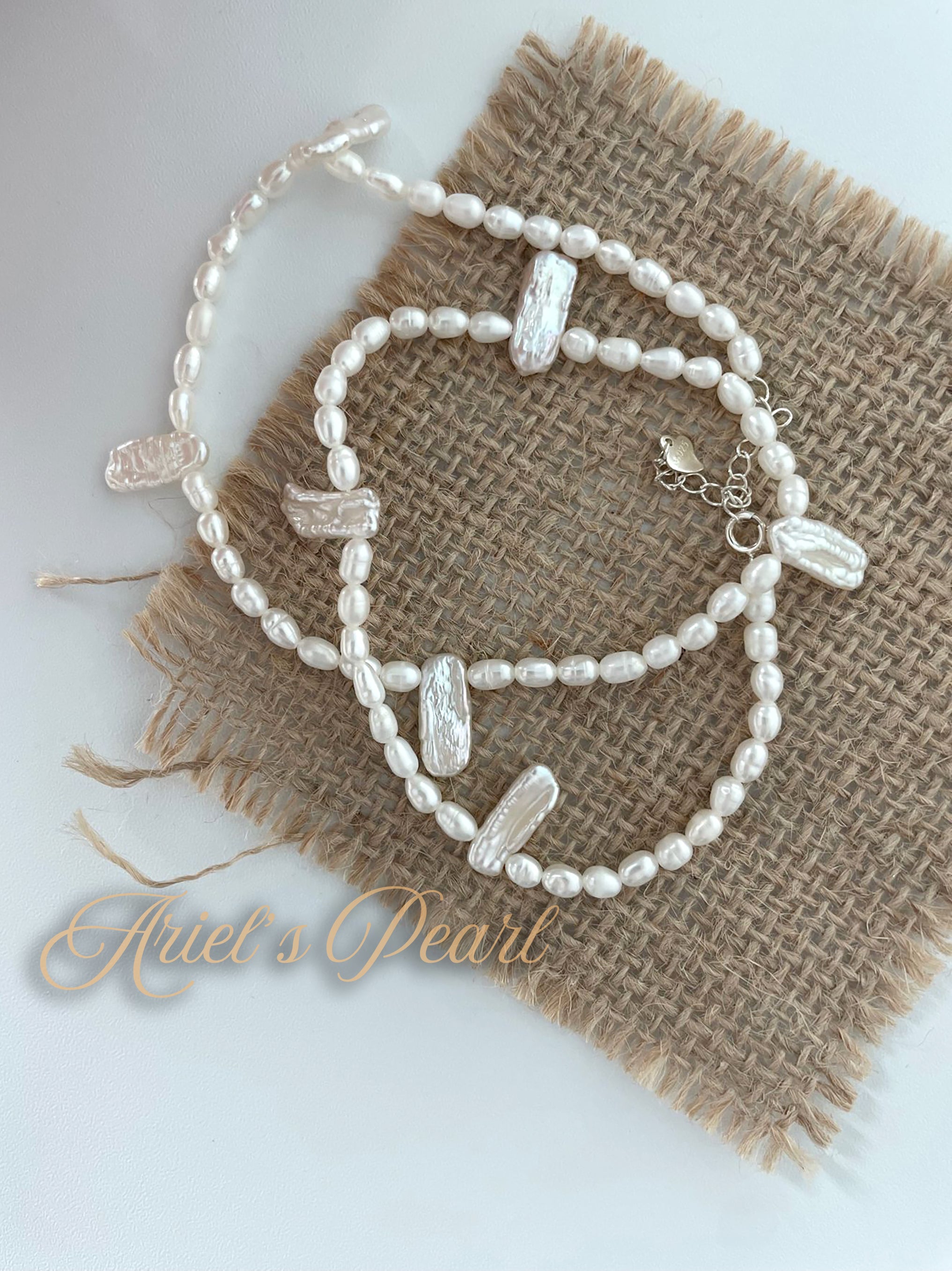 Pearl necklace on a textured fabric background with 'Ariel's Pearl' branding.