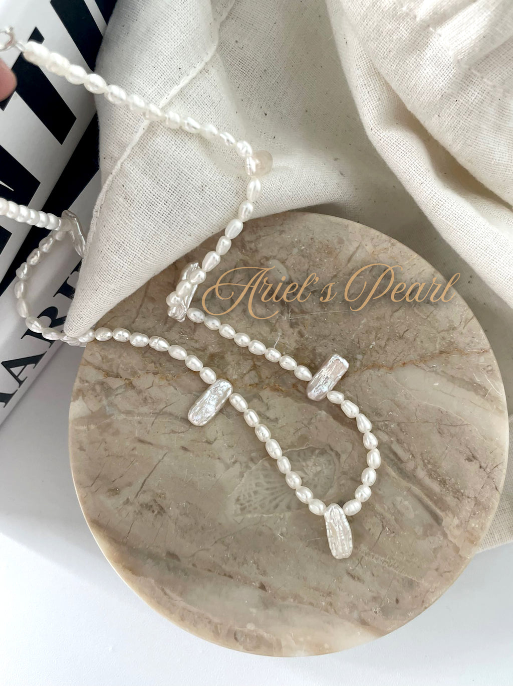 Pearl necklace on a marble surface with 'Ariel's Pearl' branding.