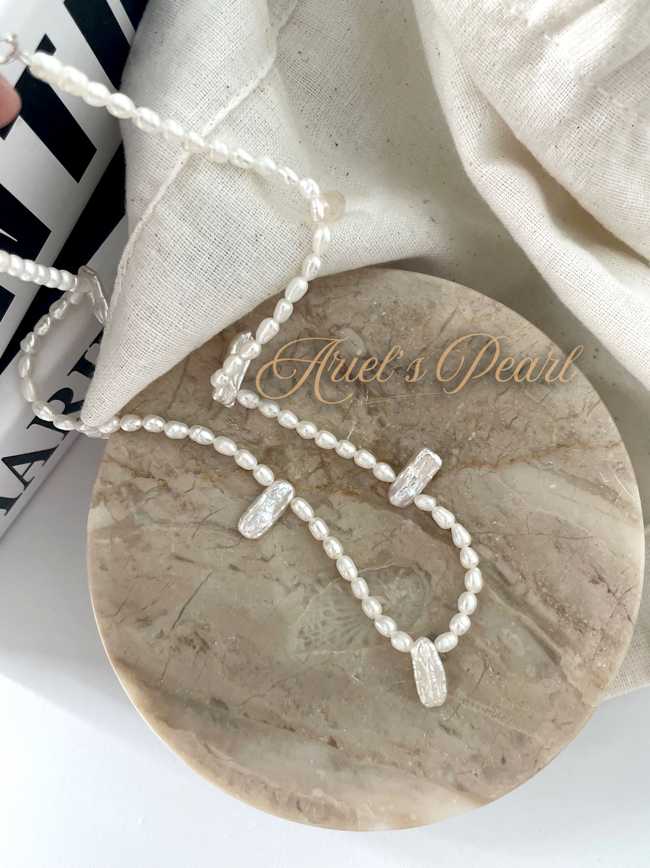 Pearl necklace on a marble surface with 'Ariel's Pearl' branding.