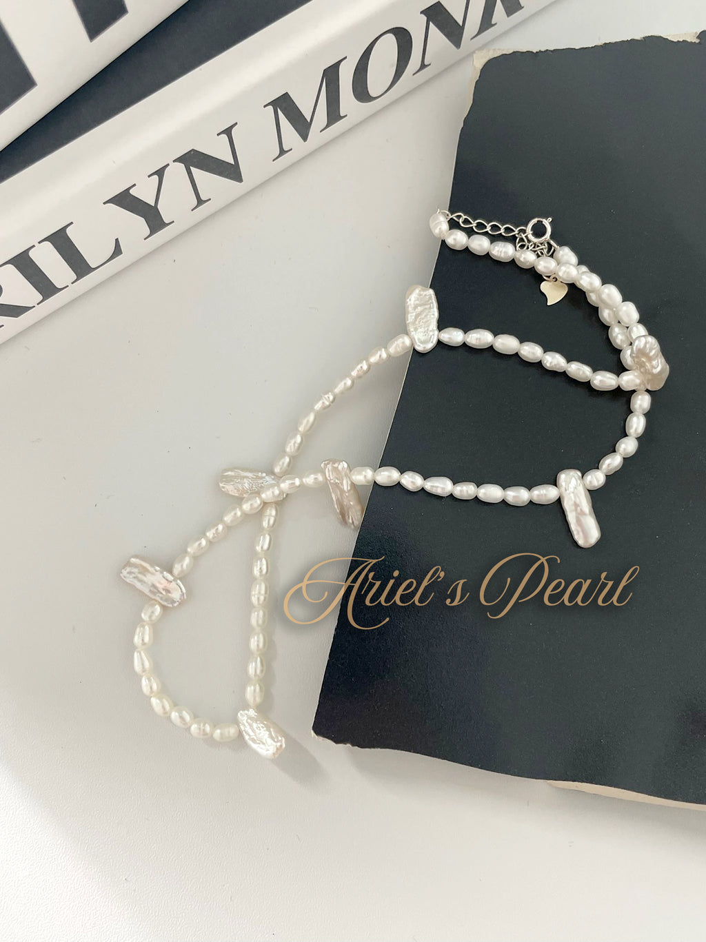 Pearl necklace on a black book with 'Ariel's Pearl' branding.