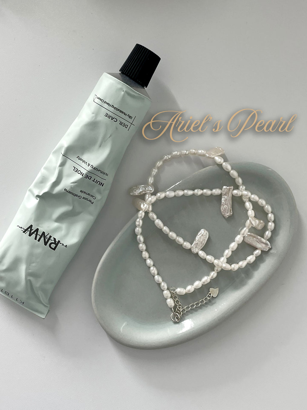 Tube of cream and pearl jewelry on a white dish with 'Ariel's Pearl' branding.