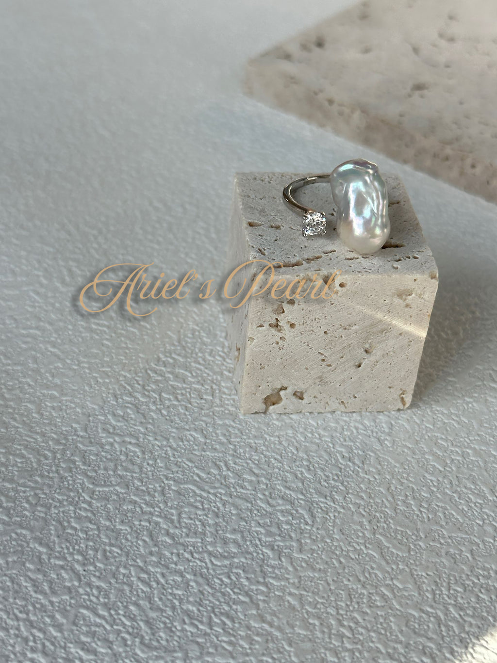 Open Pearl with zircon accents on a stone block with 'Ariel's Pearl' branding on a textured surface.