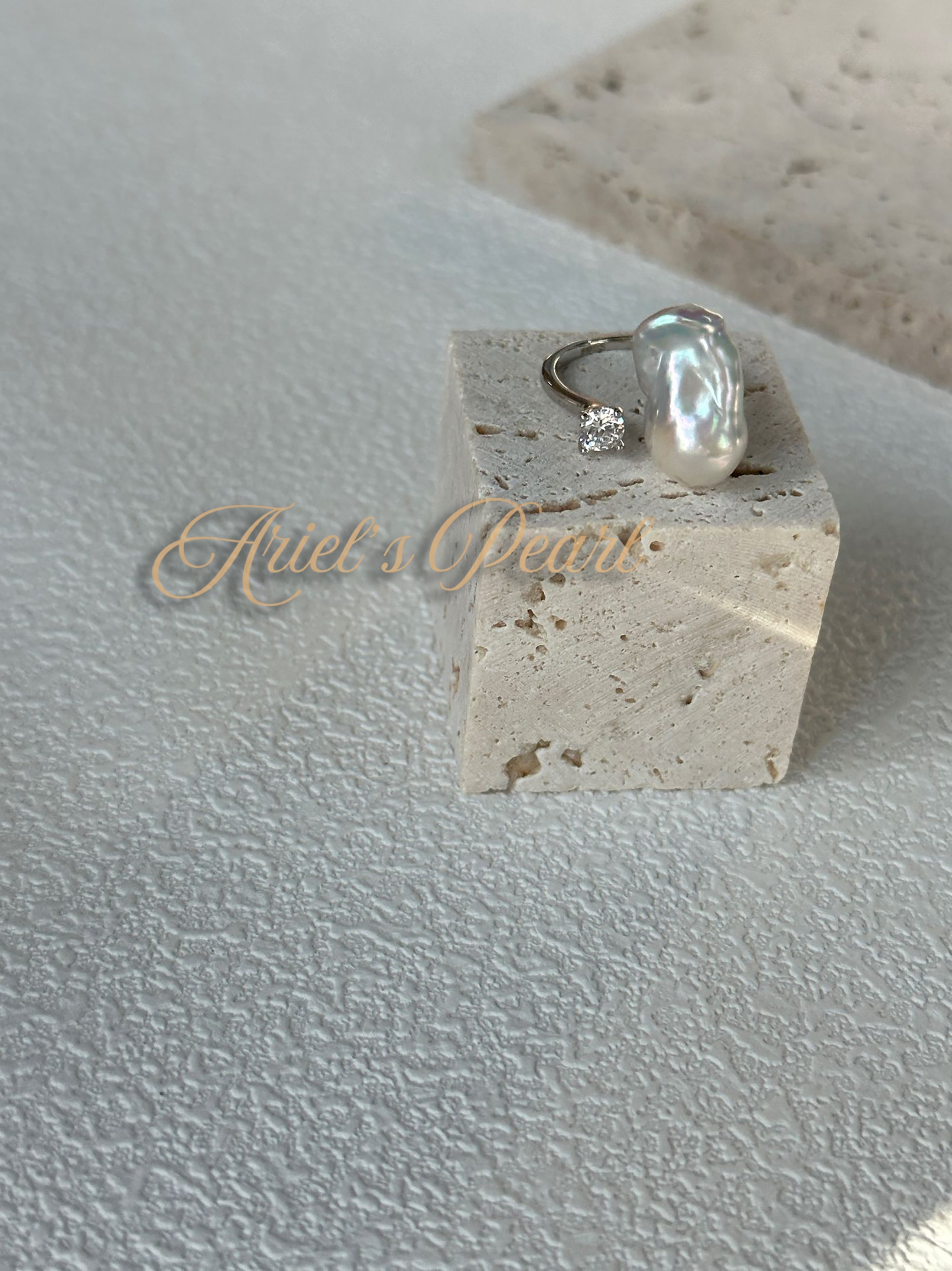 Open Pearl with zircon accents on a stone block with 'Ariel's Pearl' branding on a textured surface.