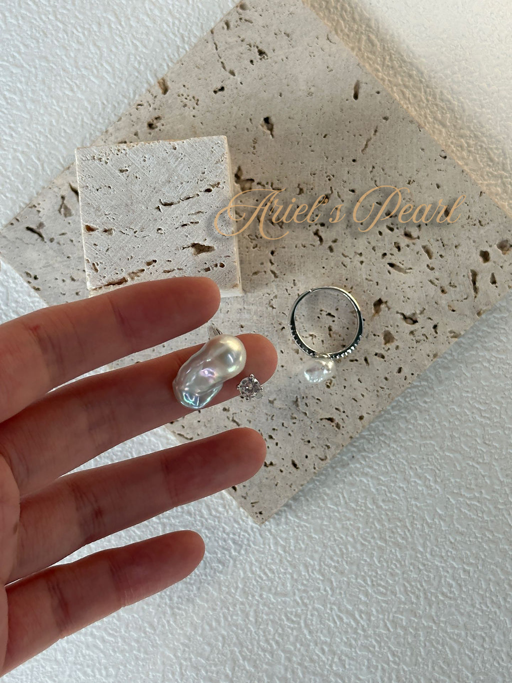 Pearl and silver ring on a hand with 'Ariel's Pearl' branded stone background