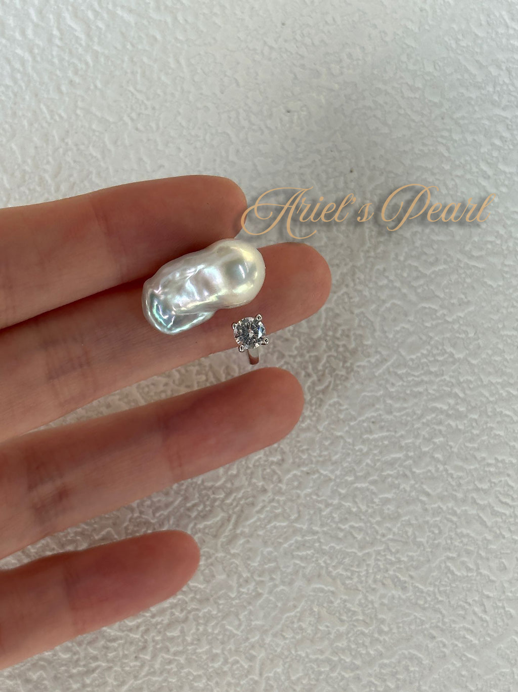 Pearl with zircon ring on a hand with 'Ariel's Pearl' branding.