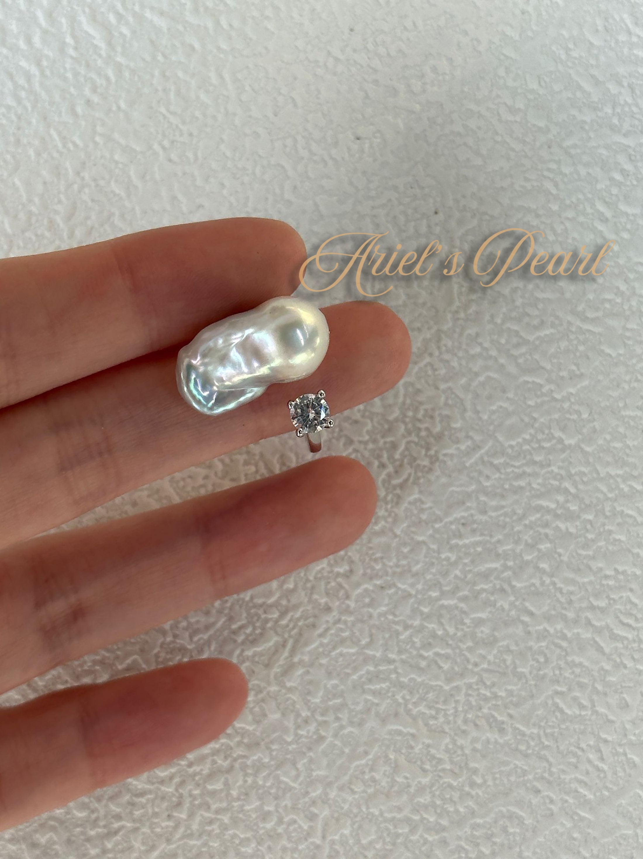 Pearl with zircon ring on a hand with 'Ariel's Pearl' branding.