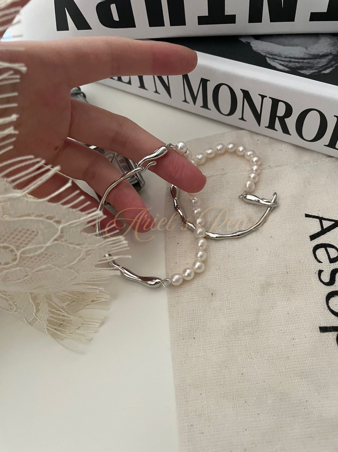 Hand wearing a silver ring with a pearl bracelet on a textured surface