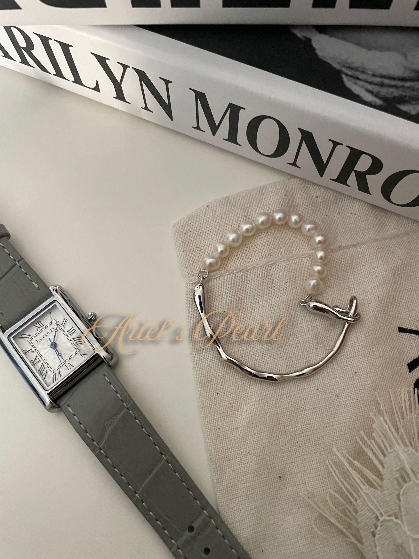 Pearl bracelet and watch on a surface with 'Marilyn Monroe' book in the background