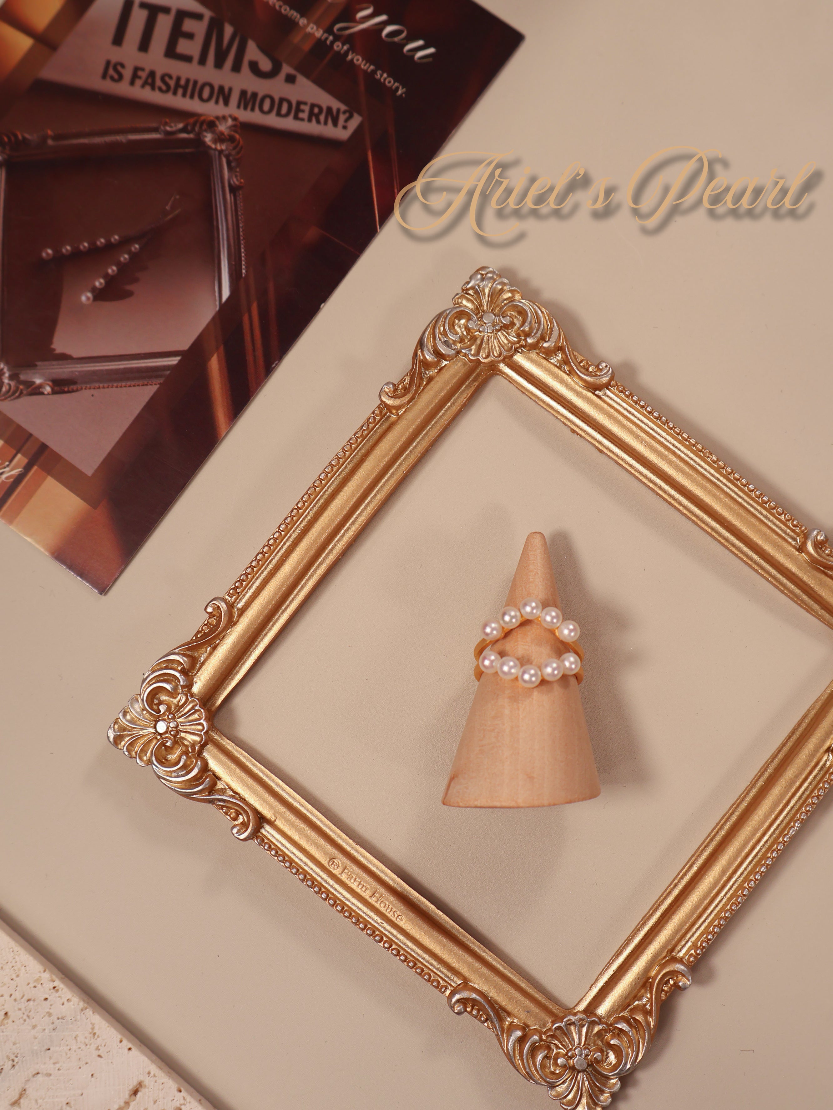 Decorative ring holder with pearls inside a gold frame on a beige surface.