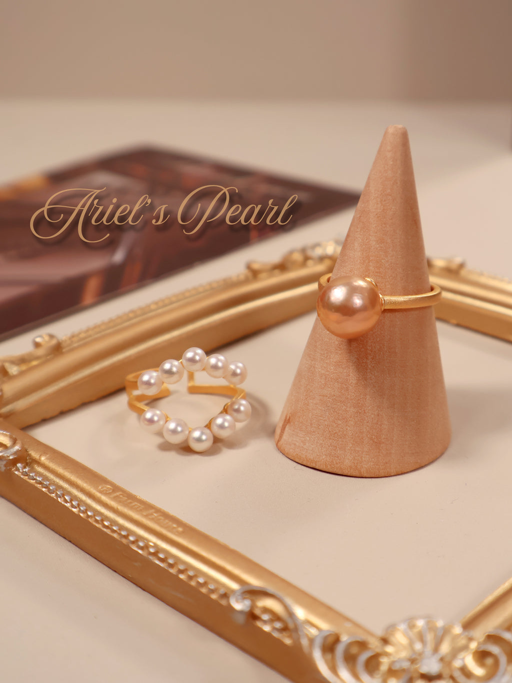Gold and pearl ring on a wooden cone with 'Ariel's Pearl' branding.