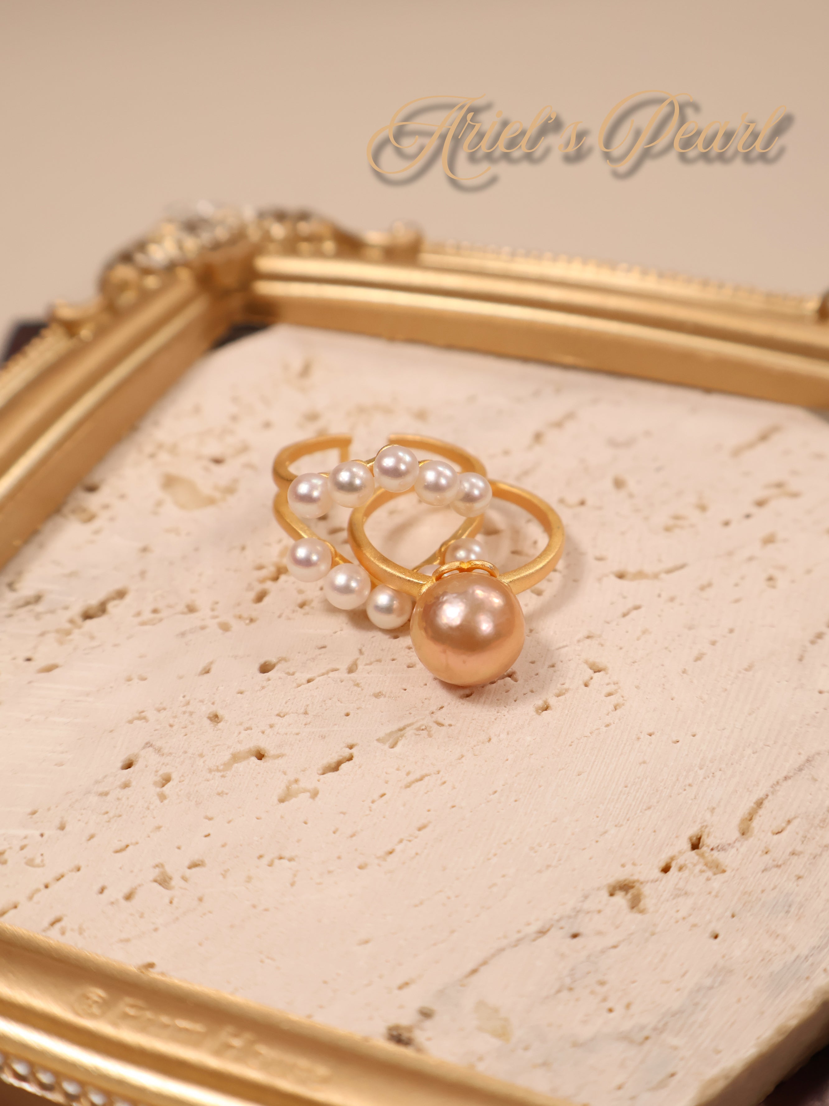 Gold ring with pearls on a beige fabric background with 'Ariel's Pearl' branding.